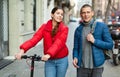 Couple are walking along the spring street. Girl with electric scooter Royalty Free Stock Photo