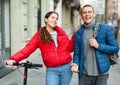 Couple are walking along the spring street. Girl with electric scooter Royalty Free Stock Photo