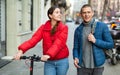 Couple are walking along the spring street. Girl with electric scooter Royalty Free Stock Photo