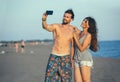Couple walking on beach at sunset taking selfie picture on mobil