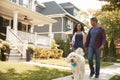 Couple Walking Dog Along Suburban Street