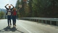 Couple walk forest highway in mountains. Hitchhikers wait car wave hands outside Royalty Free Stock Photo