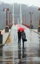 Couple walking under red umbrella on a rainy foggy day on the downtown Kyiv pedestrian city bridge