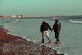 Couple walks along a UK beach in the winter