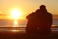 Couple watching sunset on the beach in winter Royalty Free Stock Photo