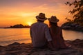 Couple watching sunset while sitting together on beach during summer tropical vacation Royalty Free Stock Photo