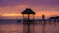 couple watching sunset on a tropical beach with wooden pier in the ocean, men and woman sunset on the beach during Royalty Free Stock Photo