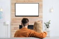 Couple watching TV on sofa in living room with decorative fireplace