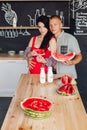 Couple with watermelon in the kitchen.They holding sliced watermelon at wooden table in modern kitchen. Royalty Free Stock Photo