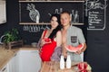 Couple with watermelon in the kitchen.They holding sliced watermelon at wooden table in modern kitchen. Royalty Free Stock Photo