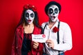 Couple wearing day of the dead costume holding happy halloween paper afraid and shocked with surprise and amazed expression, fear