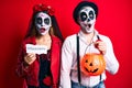 Couple wearing day of the dead costume holding pumpking and halloween paper afraid and shocked with surprise and amazed