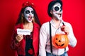 Couple wearing day of the dead costume holding pumpking and halloween paper angry and mad screaming frustrated and furious,