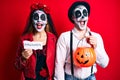 Couple wearing day of the dead costume holding pumpking and halloween paper celebrating crazy and amazed for success with open