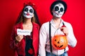 Couple wearing day of the dead costume holding pumpking and halloween paper looking at the camera blowing a kiss being lovely and