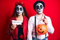 Couple wearing day of the dead costume holding pumpking and halloween paper making fish face with mouth and squinting eyes, crazy