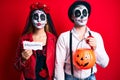 Couple wearing day of the dead costume holding pumpking and halloween paper puffing cheeks with funny face
