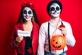 Couple wearing day of the dead costume holding pumpking and halloween paper smiling with a happy and cool smile on face