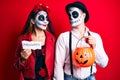 Couple wearing day of the dead costume holding pumpking and halloween paper smiling looking to the side and staring away thinking