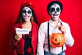 Couple wearing day of the dead costume holding pumpking and halloween paper sticking tongue out happy with funny expression