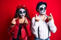 Couple wearing day of the dead costume over red doing money gesture with hands, asking for salary payment, millionaire business