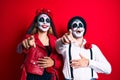 Couple wearing day of the dead costume over red laughing at you, pointing finger to the camera with hand over body, shame