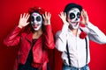 Couple wearing day of the dead costume over red smiling cheerful playing peek a boo with hands showing face