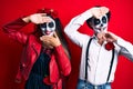 Couple wearing day of the dead costume over red smiling cheerful playing peek a boo with hands showing face