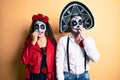 Couple wearing day of the dead costume over yellow looking stressed and nervous with hands on mouth biting nails