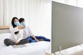 Couple wearing facial mask watching news on television while staying at home during quarantine from coronavius or covid-19