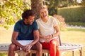 Couple Wearing Fitness Clothing Sitting On Seat Under Tree Checking Activity Monitor On Smartwatch