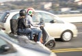 Couple wearing Italian flag helmets riding gray scooter over the city street bridge in busy traffic in motion blur