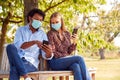 Couple Wearing Masks Meeting In Outdoor Park During Health Pandemic Looking At Mobile Phones Royalty Free Stock Photo