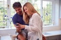 Couple Wearing Pyjamas In Kitchen Using Mobile Phone Whilst Eating Breakfast Royalty Free Stock Photo