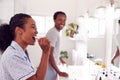 Couple Wearing Pyjamas Standing In Bathroom At Sink Brushing Teeth In The Morning