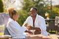 Couple Wearing Robes Outdoors Sitting With Drinks On Loungers Around Swimming Pool On Spa Day Royalty Free Stock Photo