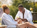 Couple Wearing Robes Outdoors Sitting With Drinks On Loungers Around Swimming Pool On Spa Day Royalty Free Stock Photo