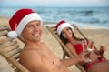 Happy couple wearing Santa hats and drinking champagne together on beach. Christmas vacation Royalty Free Stock Photo