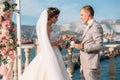 Couple in wedding arch exchange rings with lake on background, the bride with long beautiful hairs and groom in black Royalty Free Stock Photo