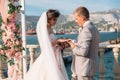 Couple in wedding arch exchange rings with lake on background, the bride with long beautiful hairs and groom in black Royalty Free Stock Photo