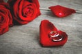 Couple wedding rings on red rose petal with red rose flower bouquet on wooden background