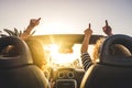 Couple of woman friends traveling and driving having a lot of fun dancing in the car with opened roof and summer vacation sunset