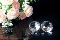 Couple of wonderful pure diamonds and bouquet of tea roses with reflection on black mirror background close up view. Jewelry Royalty Free Stock Photo