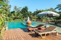 Couple of Wooden Chair under The Umbrella by The Swimming Pool surrounded by Various Type of Trees