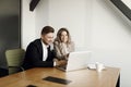 A couple working at a laptop and blueprints in their home office smile. A man and a woman discuss business matters. Royalty Free Stock Photo