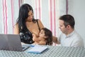 Couple works and watches laptop computer at home while baby takes mother`s breast Royalty Free Stock Photo