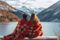 A couple wrapped in a blanket sits intimately, admiring the serene view of a mountain lake Royalty Free Stock Photo