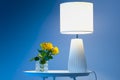 A couple of yellow roses on a white table next to a lamp against dark blue background close up floral view Royalty Free Stock Photo