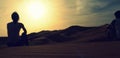 A couple of young adventurers sitting over a sand dune and enjoying an amazing sunset over the red dunes sea of Erg Chebbi