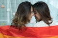 Couple of young Asian lesbian women facing each other covering themselves with LGBT rainbow flag